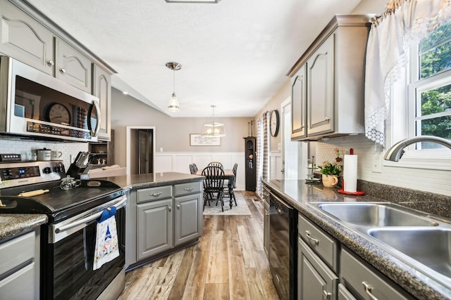 kitchen with gray cabinets, a sink, dark countertops, stainless steel appliances, and wainscoting