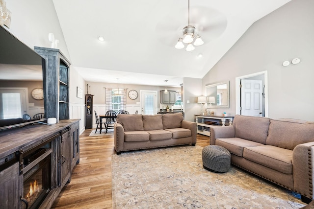 living room featuring high vaulted ceiling, light wood finished floors, and wainscoting