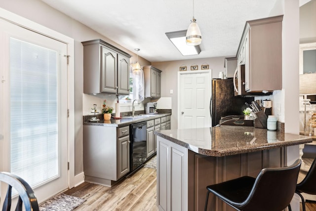 kitchen featuring light wood finished floors, a peninsula, gray cabinets, a sink, and black appliances