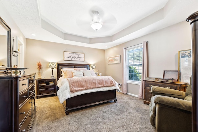 bedroom featuring baseboards, a raised ceiling, light carpet, and ceiling fan