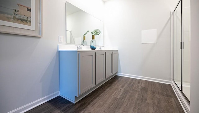 bathroom with double vanity, a stall shower, baseboards, and wood finished floors