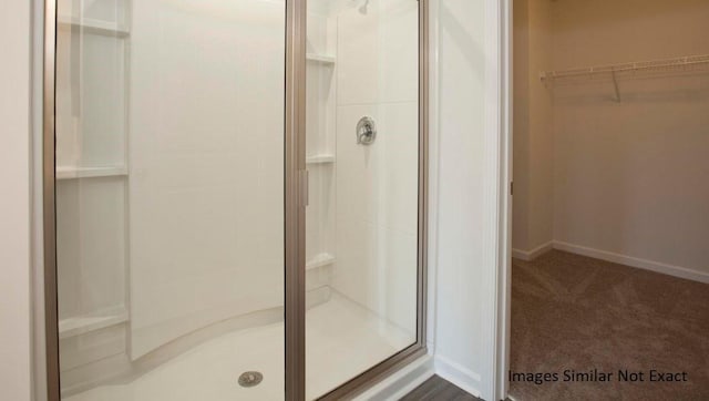 bathroom featuring a spacious closet, a shower stall, and baseboards