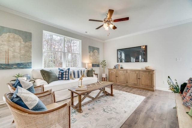 living area with a ceiling fan, light wood-type flooring, baseboards, and ornamental molding