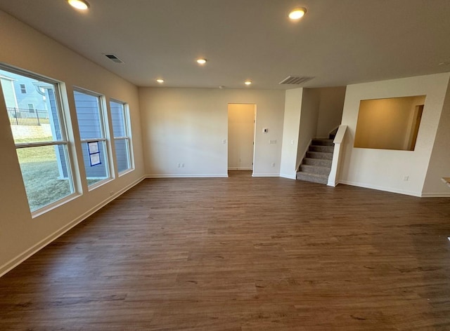 empty room featuring a wealth of natural light, visible vents, stairway, and dark wood-style flooring