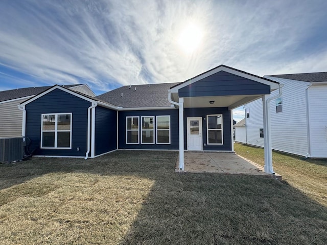 back of property featuring an attached carport, central AC, a shingled roof, a patio area, and a lawn