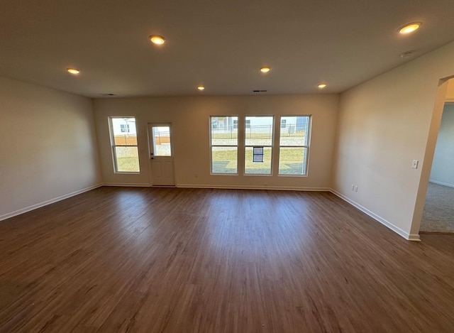 unfurnished living room featuring dark wood finished floors, baseboards, and a wealth of natural light