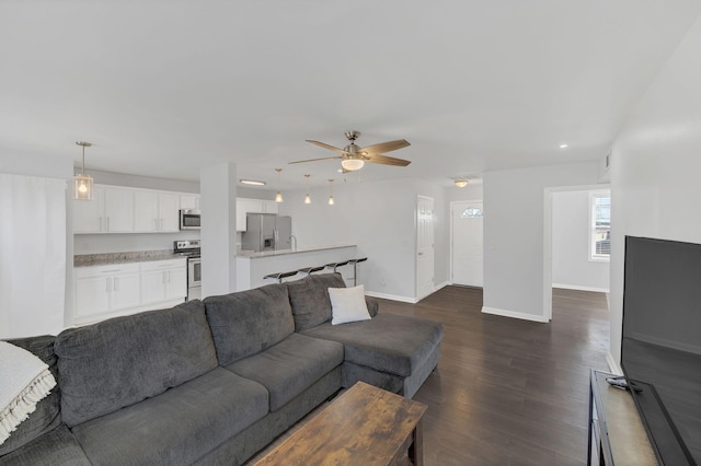 living room with baseboards, dark wood-type flooring, and a ceiling fan