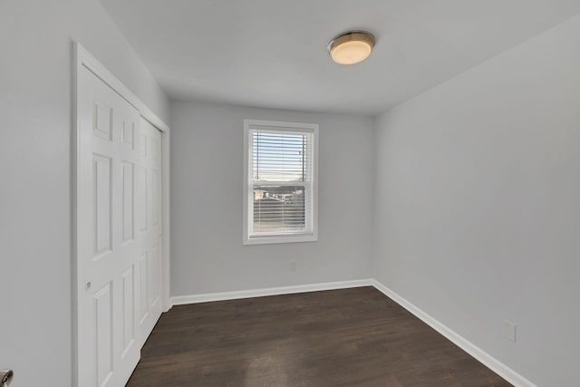 unfurnished bedroom featuring dark wood-style floors, baseboards, and a closet