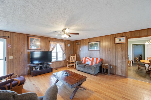 living area featuring baseboards, ceiling fan, wood walls, light wood-style flooring, and a textured ceiling