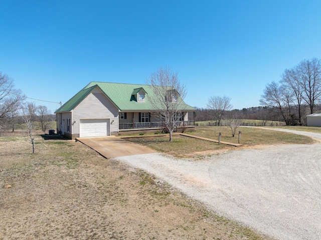 view of front of property with covered porch, a front lawn, a garage, dirt driveway, and metal roof