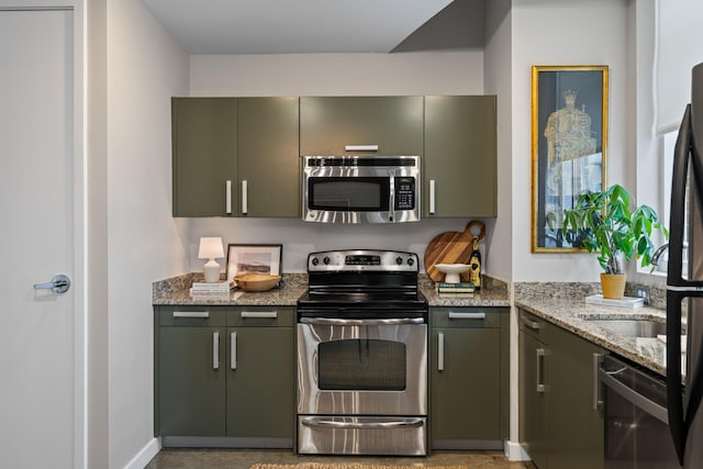 kitchen with green cabinets, light stone counters, baseboards, and stainless steel appliances