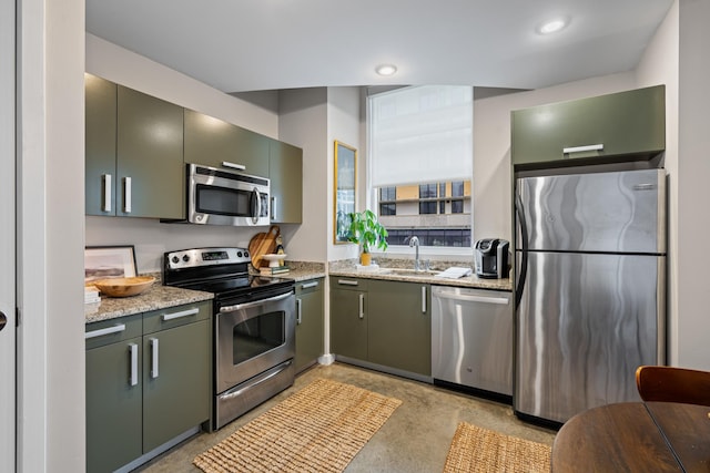 kitchen with finished concrete flooring, green cabinets, light stone countertops, appliances with stainless steel finishes, and a sink