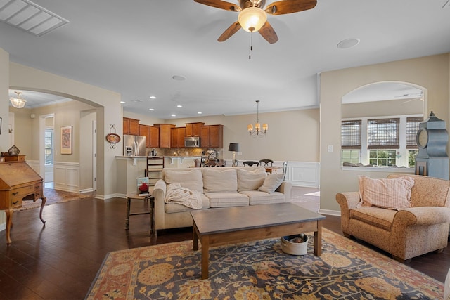 living area with dark wood-type flooring, ceiling fan with notable chandelier, visible vents, and wainscoting