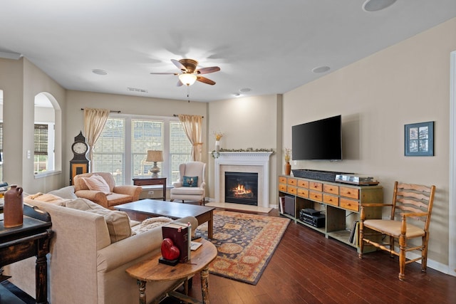 living room with visible vents, baseboards, dark wood-style floors, a glass covered fireplace, and a ceiling fan