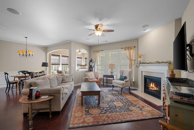 living area with a glass covered fireplace, dark wood-type flooring, ceiling fan with notable chandelier, and a healthy amount of sunlight