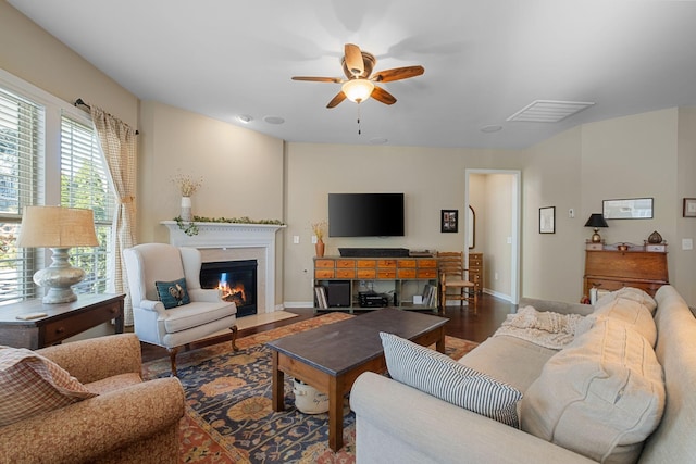 living room featuring a ceiling fan, a fireplace with flush hearth, wood finished floors, and baseboards