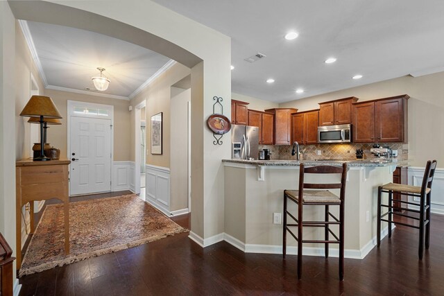 kitchen featuring visible vents, a breakfast bar, stainless steel appliances, arched walkways, and a peninsula