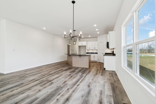 kitchen featuring dark countertops, baseboards, an inviting chandelier, wood finished floors, and white cabinetry