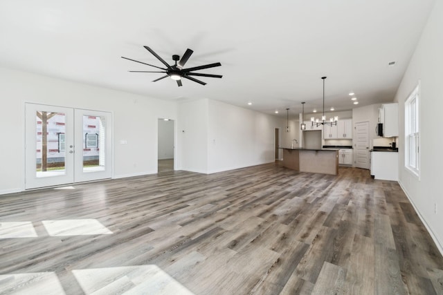 unfurnished living room with a wealth of natural light, ceiling fan with notable chandelier, french doors, and wood finished floors