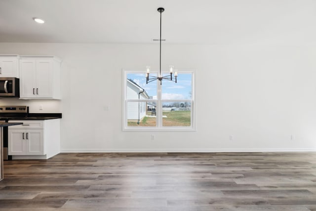 unfurnished dining area with an inviting chandelier, recessed lighting, wood finished floors, and baseboards