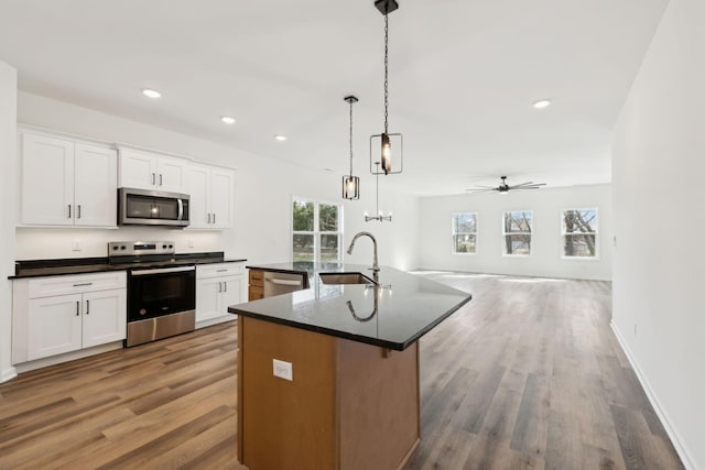 kitchen featuring open floor plan, a center island with sink, stainless steel appliances, white cabinetry, and a sink