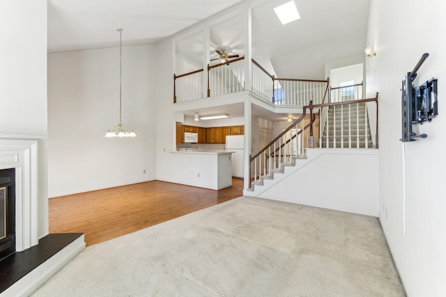 unfurnished living room with high vaulted ceiling, wood finished floors, a glass covered fireplace, stairway, and carpet