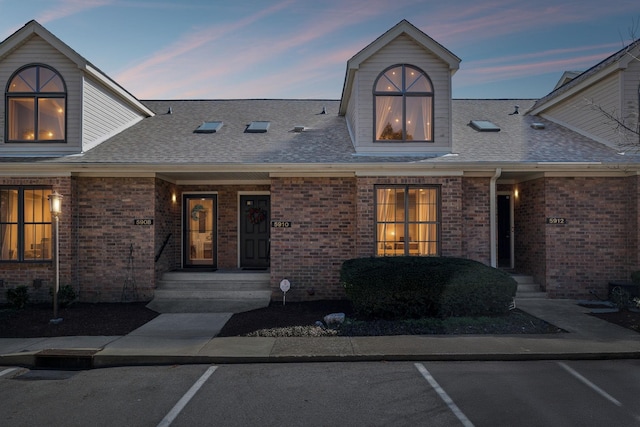 view of front of house featuring brick siding, uncovered parking, and a shingled roof