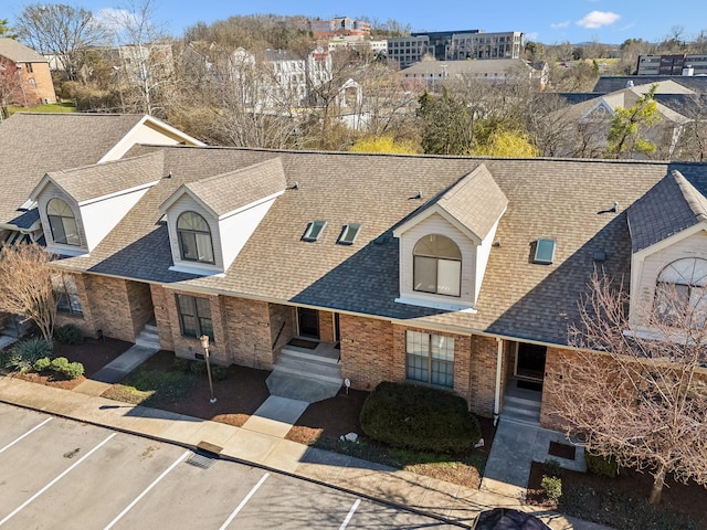 view of front of house featuring uncovered parking, a residential view, brick siding, and roof with shingles