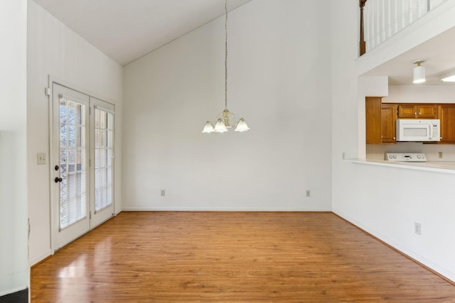 unfurnished dining area with light wood-style floors, baseboards, a high ceiling, and a chandelier