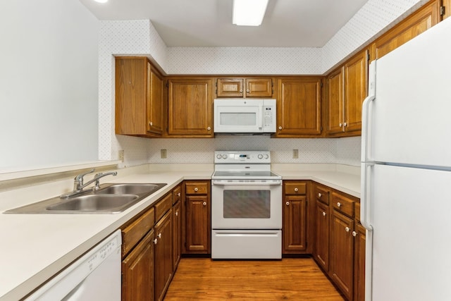 kitchen with a sink, wallpapered walls, wood finished floors, white appliances, and light countertops