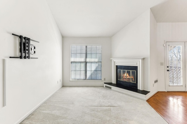 carpeted living room with a glass covered fireplace, baseboards, visible vents, and wood finished floors