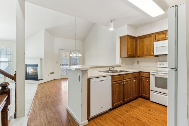 kitchen featuring white appliances, a peninsula, a sink, a glass covered fireplace, and brown cabinets