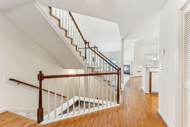 stairway with a notable chandelier, a glass covered fireplace, baseboards, and wood finished floors