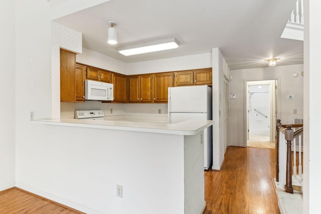 kitchen with light wood-type flooring, brown cabinets, white appliances, a peninsula, and light countertops