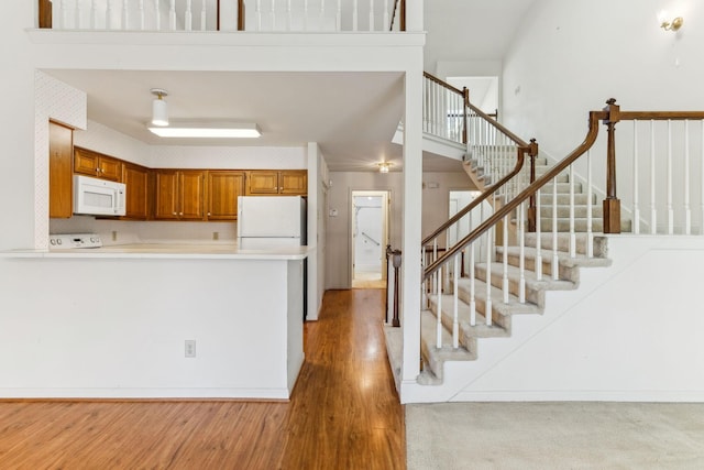 kitchen featuring light countertops, light wood-type flooring, brown cabinets, a peninsula, and white appliances