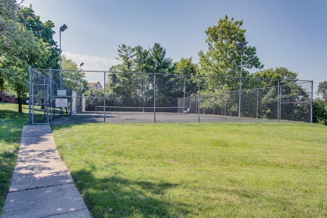 view of tennis court with a yard and fence