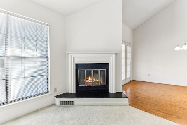 unfurnished living room with visible vents, baseboards, lofted ceiling, and a glass covered fireplace