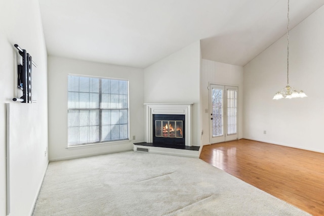 unfurnished living room with wood finished floors, visible vents, an inviting chandelier, vaulted ceiling, and a glass covered fireplace