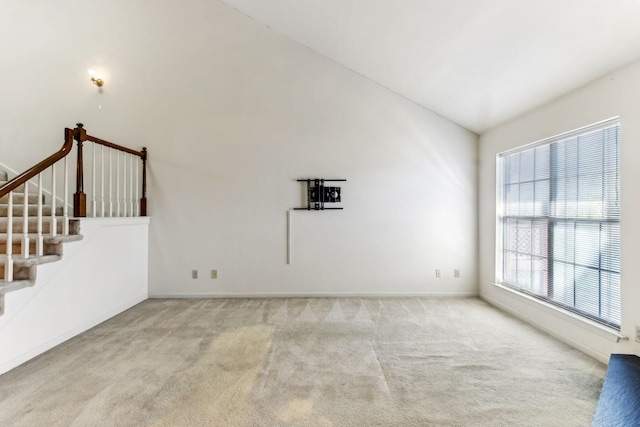 carpeted empty room featuring stairway, high vaulted ceiling, and baseboards