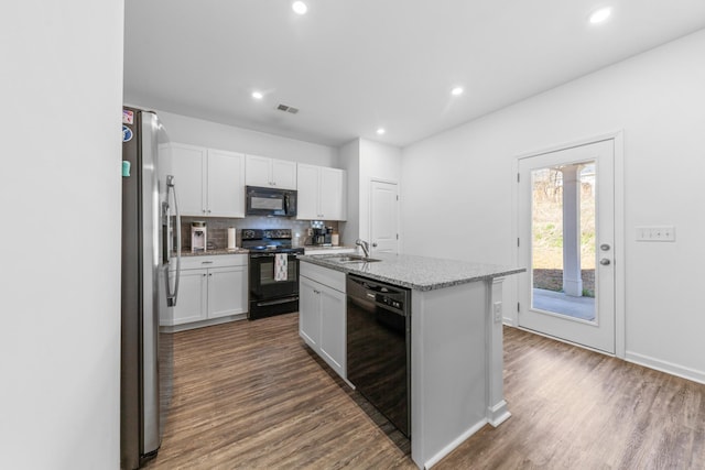 kitchen featuring tasteful backsplash, visible vents, dark wood-type flooring, black appliances, and a sink