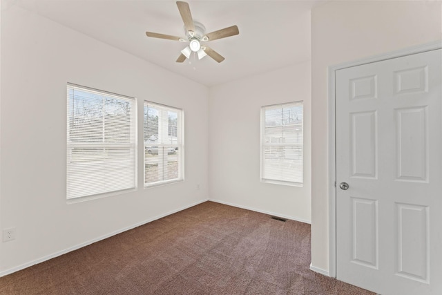 spare room featuring dark colored carpet, baseboards, plenty of natural light, and a ceiling fan