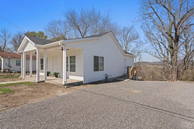 view of side of home with a patio area, driveway, ceiling fan, and roof with shingles