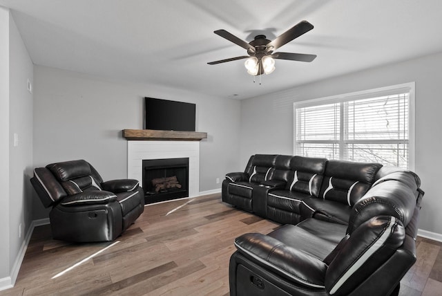 living room featuring baseboards, a fireplace, wood finished floors, and a ceiling fan