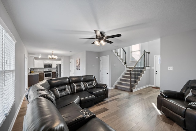 living area with stairway, ceiling fan with notable chandelier, baseboards, a textured ceiling, and wood finished floors
