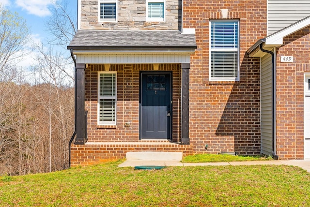 property entrance with a lawn, a shingled roof, and brick siding