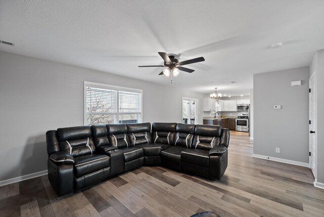 living area featuring baseboards, ceiling fan with notable chandelier, light wood-style floors, and visible vents