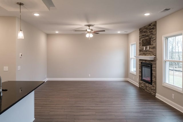 unfurnished living room with dark wood finished floors, a stone fireplace, plenty of natural light, and visible vents