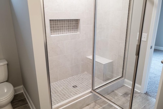 bathroom with a shower stall, toilet, and baseboards