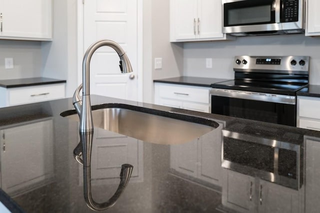 kitchen featuring a sink, dark stone countertops, white cabinets, and stainless steel appliances