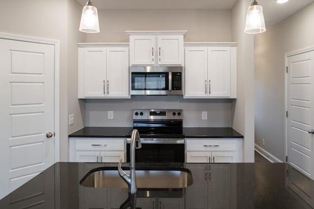 kitchen featuring dark countertops, pendant lighting, appliances with stainless steel finishes, white cabinetry, and a sink